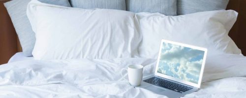 Laptop pc and cup of coffee on the bed with a lot of pillows