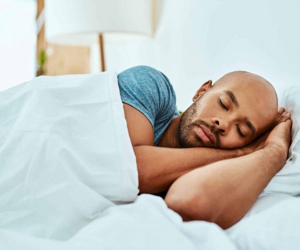 Relax, sleeping and man in bed, home and wellness with peace, comfortable or happiness. Male person, African or guy in a bedroom, healthy rest or dreaming with comfort, sleepy or tired with a blanket.